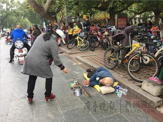 泰安一中北臨，一名乞丐躺在地上，來往市民不時(shí)地給他施捨一些零錢。